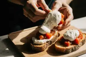 Assembling burrata bruschetta by topping toasted bread with tomato mixture and burrata cheese