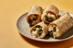 Plate of tamales de rajas con queso with roasted green chile and melted cheese in corn husks