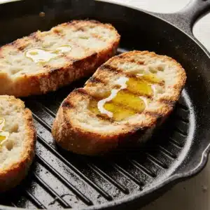 Rustic bread slices toasting on a grill pan with olive oil for burrata bruschetta