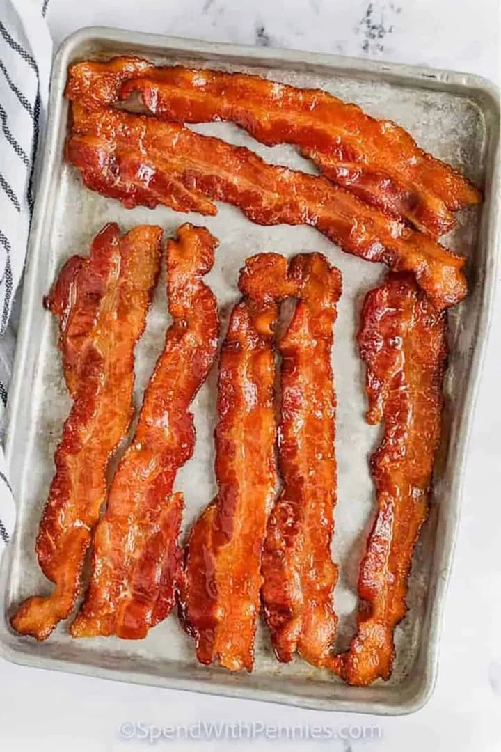 How to Cook Bacon in the Oven 1 Crispy bacon cooking in the oven on a baking sheet.